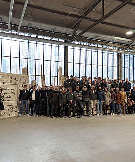 Mitarbeiter stehten in einer Werkhalle vor einer Wand mit Handabdrücken