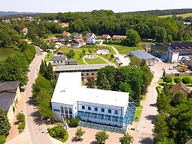 Weißes Bürogebäude mit Glasvordach in einer grünen Landschaft mit Straßen und Wohnhäusern