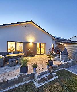 Abendliche Terrasse mit Sitzmöbeln, Pflanzen und beleuchtetem Haus im Hintergrund