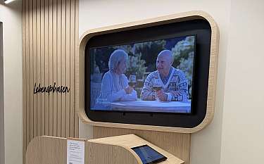 Holzverkleidete Informationsstation mit Bildschirm und Bedienpult in einem modernen Innenraum.