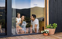 Glasfenster mit Familie drinnen, Mutter hält Kind, Vater sitzt daneben, bepflanzeter Garten