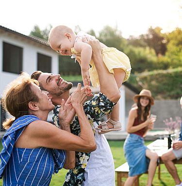 Drei Generationen Familie spielen mit Baby im Garten vor Haus