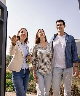 Immobilienmaklerin führt Paar durch Gartentor zu einem Haus